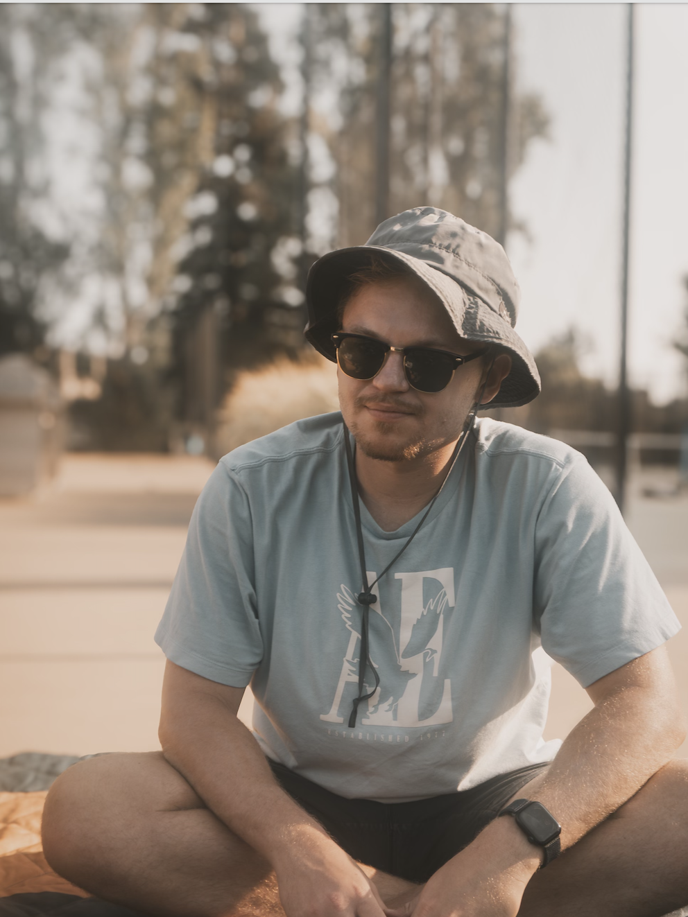 Brett sitting criss cross in a bucket hat and sunglasses looking fly