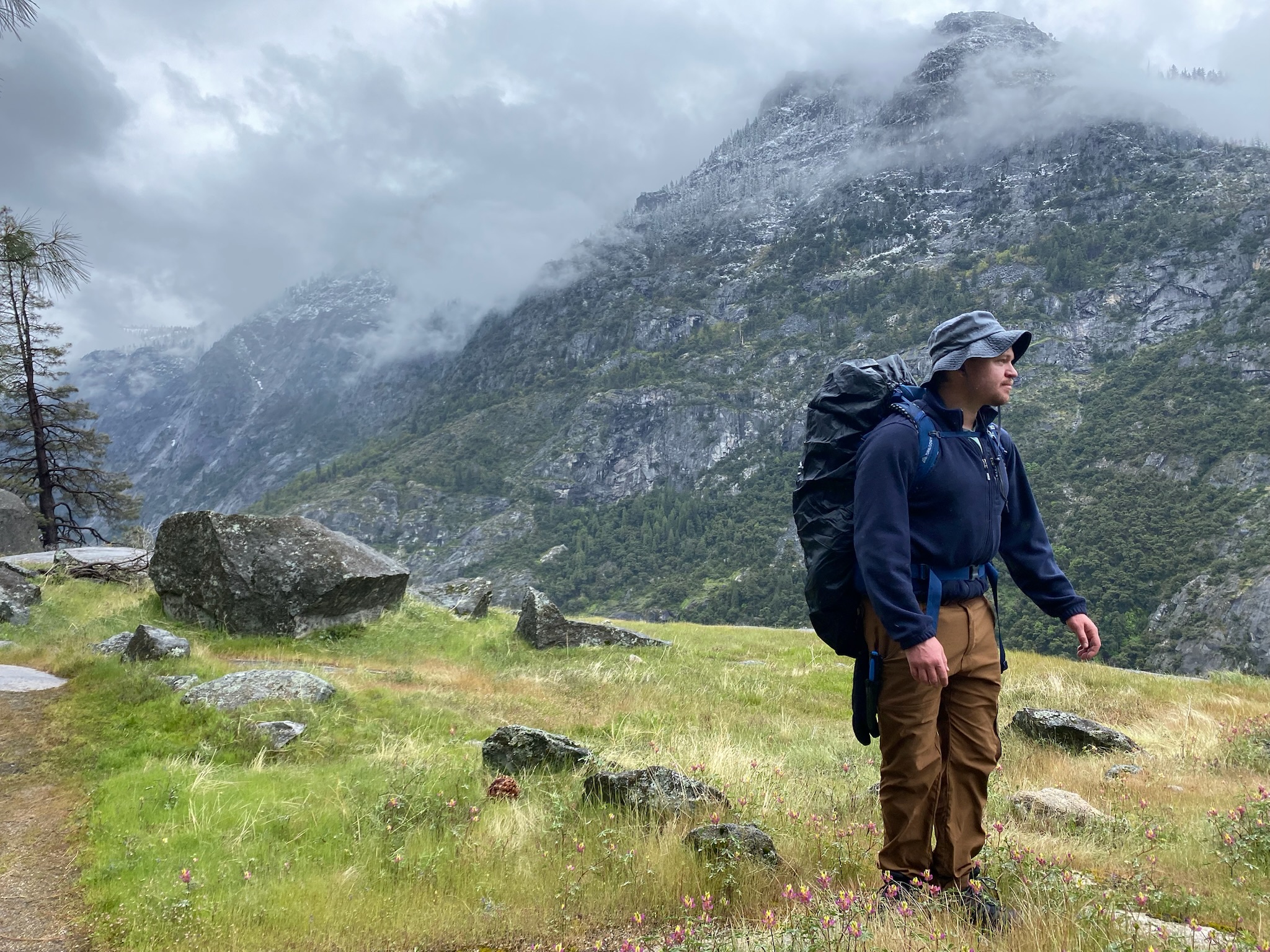 Brett backpacking on a grassy cliff with mountains in the background (Yosemite)